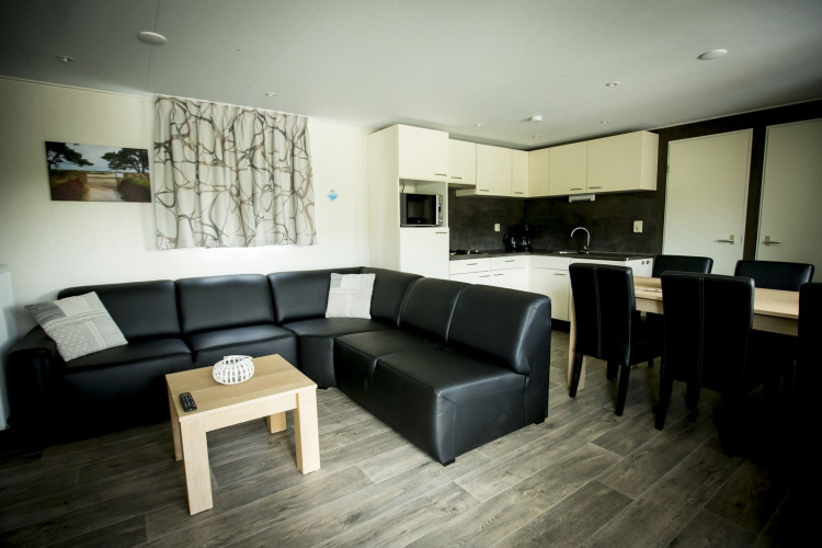 Sala moderna con sofá de cuero negro, mesa de comedor y cocina en Dune Lodge, Holiday Park Duinhoeve, Países Bajos.