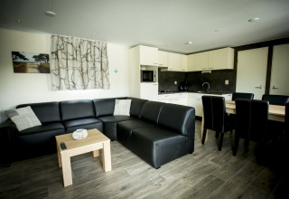 Sala moderna con sofá de cuero negro, mesa de comedor y cocina en Dune Lodge, Holiday Park Duinhoeve, Países Bajos.