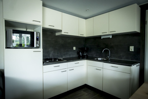 Cocina moderna en la Dune Lodge del Holiday Park Duinhoeve, Países Bajos, con armarios blancos y encimeras oscuras.