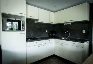 Cocina moderna en la Dune Lodge del Holiday Park Duinhoeve, Países Bajos, con armarios blancos y encimeras oscuras.