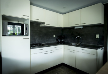 Moderne keuken in Dune Lodge op Holiday Park Duinhoeve, Nederland met witte kasten en een donkere werkblad.
