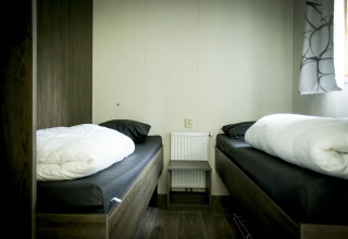 Eenvoudige tweepersoonskamer met twee aparte bedden in Dune Lodge, Holiday Park Duinhoeve, Nederland.