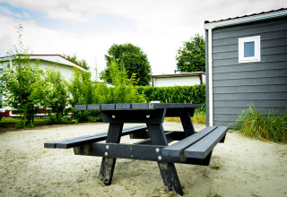 Banco de picnic negro sobre arena junto a Dune Lodge en Holiday Park Duinhoeve, Países Bajos, con cabañas.