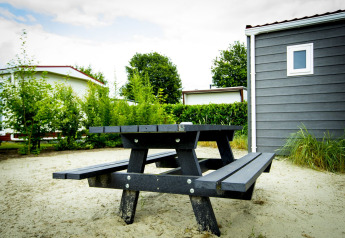 Banco de picnic negro sobre arena junto a Dune Lodge en Holiday Park Duinhoeve, Países Bajos, con cabañas.