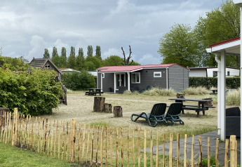 Buitenaanzicht van de Dune Lodge bij Holiday Park Duinhoeve in Nederland, met tuin en zitplaatsen.
