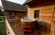 Zwei Personen entspannen sich im Außen-Whirlpool auf der Holzterrasse einer Lodge im Heydehuis, Sandberghe.