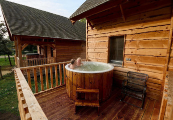 Twee personen genieten van een buitenjacuzzi op het houten terras van een lodge bij Heydehuis, Sandberghe.