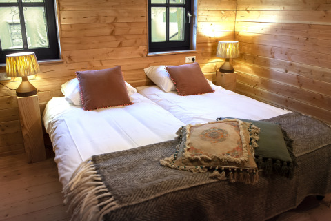 Habitación acogedora en Heydehuis glamping con cama doble, paredes de madera y cálidas lámparas de noche.