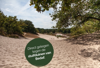 Sandede bakker ved Bedafs klitter, set fra en glampingplads omgivet af grønne træer og blå himmel.