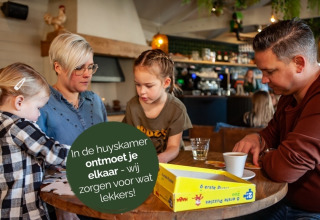 Een gezin speelt samen een gezelschapsspel in een knusse huiskamer bij een glampingverblijf.
