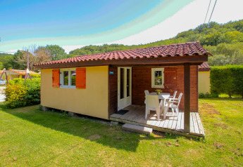 Et lyst chalet med terrasse og havemøbler på grøn græsplæne ved La Draille, Frankrig, set i solskin.