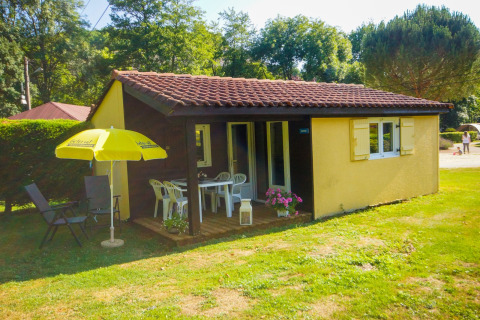 Chalet Borrèze en La Draille, Francia, con porche, muebles de jardín y una sombrilla amarilla sobre césped.