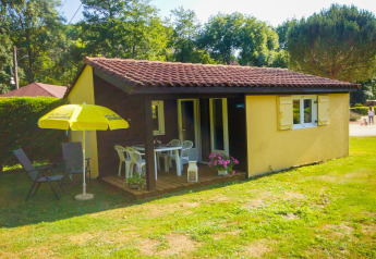 Chalet Borrèze en La Draille, Francia, con porche, muebles de jardín y una sombrilla amarilla sobre césped.