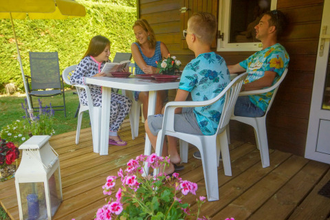 En familie sidder og hygger sig på terrassen ved Chalet Borrèze, La Draille i Frankrig, omgivet af blomster.