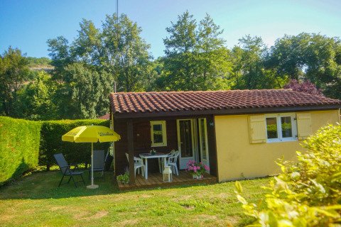 Hyggelig Chalet Borrèze-lodge ved La Draille i Frankrig, omgivet af haver og grønne træer under blå himmel.