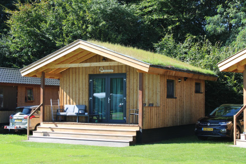 Pequeña casa de madera con techo verde llamada Cuckoo's Nest en Camping de Koeksebelt, Países Bajos, con coches.