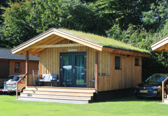 Tiny wooden house with grass roof called Cuckoo's Nest at Camping de Koeksebelt, Netherlands, with cars nearby.