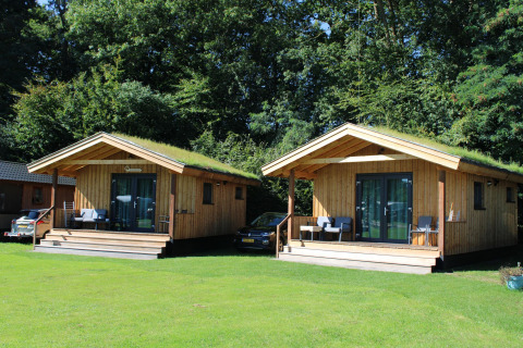 To små træhytter med græs på taget, beliggende i grønne omgivelser ved Camping de Koeksebelt, Holland.