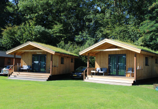 To små træhytter med græs på taget, beliggende i grønne omgivelser ved Camping de Koeksebelt, Holland.