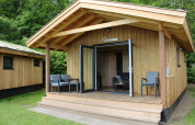 Tiny house Cuckoo's Nest bij Camping de Koeksebelt in Nederland, met houten veranda en stoelen buiten.