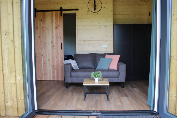 Sala moderna con sofá, mesa y paredes de madera en la tiny house Cuckoo's Nest en Koeksebelt.