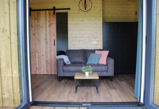 Sala moderna con sofá, mesa y paredes de madera en la tiny house Cuckoo's Nest en Koeksebelt.