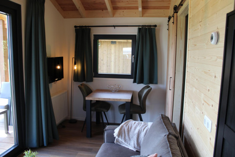 Coin salon du tiny house Cuckoo's Nest au Camping de Koeksebelt, Pays-Bas, avec canapé, table et rideaux verts.