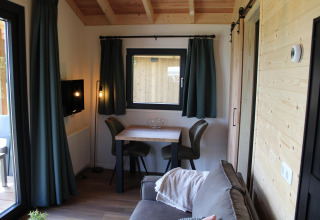 Coin salon du tiny house Cuckoo's Nest au Camping de Koeksebelt, Pays-Bas, avec canapé, table et rideaux verts.