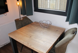 Small dining nook with wooden table, two chairs and a metal fruit bowl at Cuckoo's Nest, Camping de Koeksebelt.