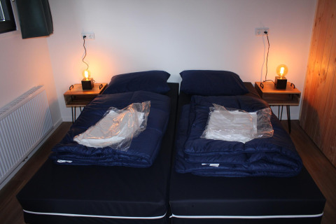 Deux lits simples dans la tiny house Cuckoo's Nest au Camping de Koeksebelt, Pays-Bas, avec tables de nuit.