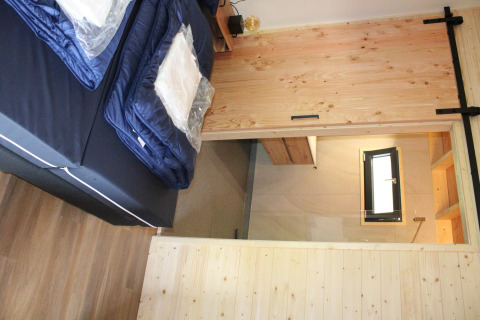 Vista interior de la tiny house Cuckoo's Nest en Camping de Koeksebelt, Países Bajos, con cama y puerta.