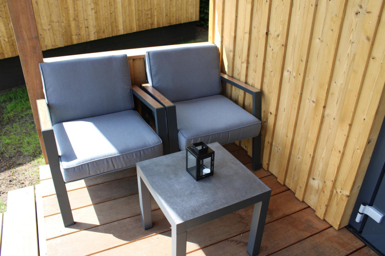 Two grey outdoor chairs and a table with a lantern on the deck of Cuckoo's Nest tiny house in the Netherlands.