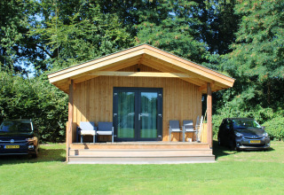 Tiny house Cuckoo's Nest au Camping de Koeksebelt aux Pays-Bas, avec deux voitures et chaises devant.