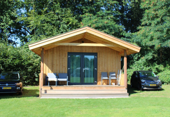 Tiny house Cuckoo's Nest bij Camping de Koeksebelt in Nederland met twee auto's en stoelen vooraan.