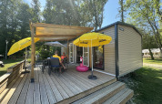 Terraza exterior del Mobilhome Toulouse en La Draille, Francia, con sombrillas y personas relajándose.