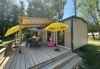 Outdoor deck of Mobilhome Toulouse at La Draille, France, with umbrellas and people relaxing on chairs.