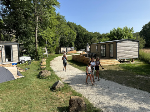 Vacation lodges at Mobilhome Toulouse, La Draille, France, with people walking on paths surrounded by nature.