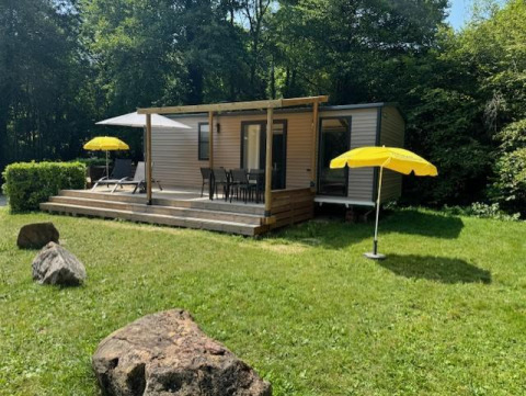 Mobilhome Toulouse en La Draille, Francia, con terraza, sombrillas amarillas y césped verde frente al bosque.