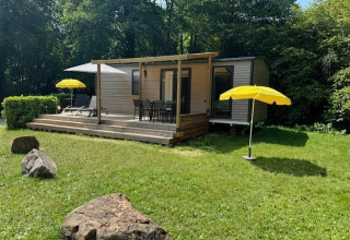 Mobilhome Toulouse en La Draille, Francia, con terraza, sombrillas amarillas y césped verde frente al bosque.