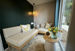 Modern lodge lounge at Mobilhome Toulouse, La Draille, France, with bright sofas, accent pillows, and flowers.
