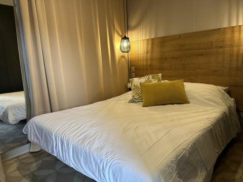 Dormitorio moderno en Mobilhome Toulouse, La Draille, Francia, con cabecero de madera y luz colgante cálida.