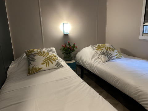 Dos camas individuales con sábanas blancas y cojines de hojas, flores, lámpara, Mobilhome Toulouse en La Draille.