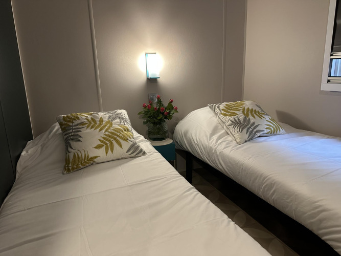 Zwei Einzelbetten mit weißen Decken und Blätterkissen, Blumen auf Nachttisch, Mobilhome Toulouse.