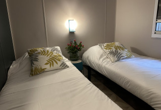 Dos camas individuales con sábanas blancas y cojines de hojas, flores, lámpara, Mobilhome Toulouse en La Draille.