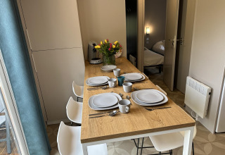 Ein Esstisch in einer Lodge ist für vier Personen gedeckt, mit Blumen und Blick ins Schlafzimmer.