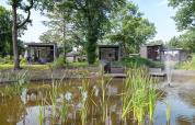Cabañas modernas junto a un estanque con una fuente y árboles en Landgoed de Scheleberg, Países Bajos.