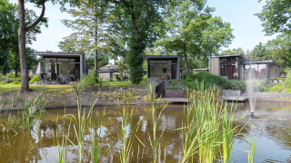Modern lodges by a pond with a fountain and trees at Landgoed de Scheleberg in the Netherlands.
