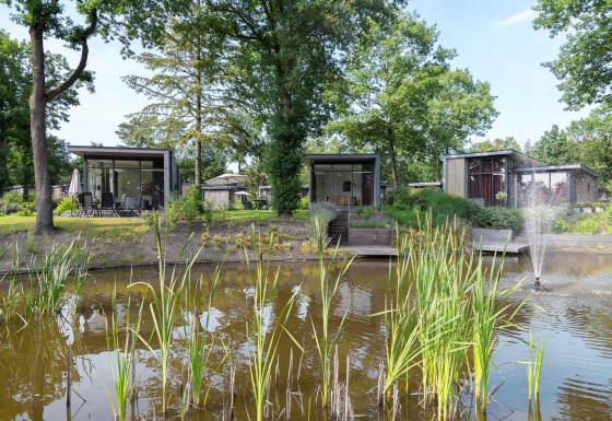 Moderne Lodges am Teich mit Springbrunnen und Bäumen im Landgoed de Scheleberg, Niederlande.