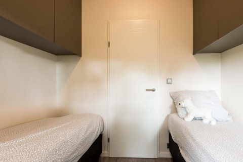 Slaapkamer met twee eenpersoonsbedden, wit beddengoed en een knuffelbeer in Module II op Landgoed de Scheleberg, Nederland.