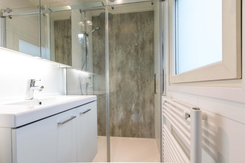 Baño moderno con ducha de vidrio, lavabo blanco y ventana en Lodge Module II en los Países Bajos.